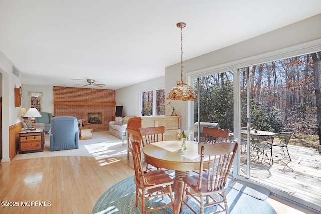 dining room featuring a brick fireplace, light wood-style flooring, visible vents, and ceiling fan