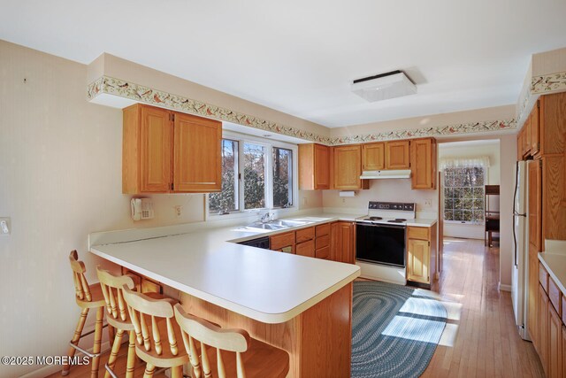 kitchen with under cabinet range hood, plenty of natural light, white appliances, and a peninsula