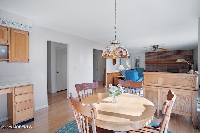 dining room featuring light wood-style flooring, a fireplace, and ceiling fan