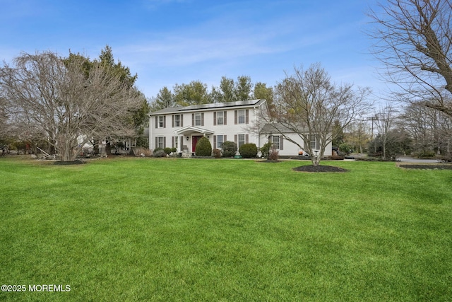 colonial house featuring roof mounted solar panels and a front lawn