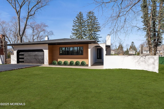 view of front facade with aphalt driveway, a chimney, a front yard, and a garage