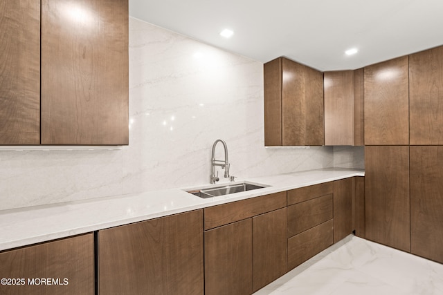 kitchen with backsplash, light countertops, marble finish floor, modern cabinets, and a sink