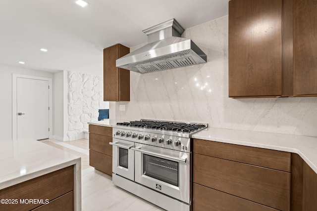 kitchen featuring light countertops, wall chimney range hood, tasteful backsplash, and range with two ovens