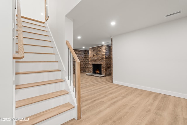 stairs featuring visible vents, baseboards, recessed lighting, a fireplace, and wood finished floors