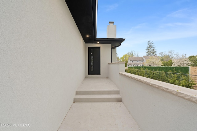 view of exterior entry with a chimney, a balcony, and stucco siding