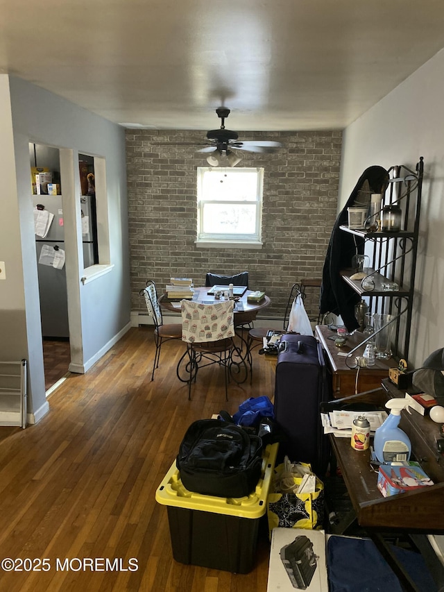 dining area featuring brick wall, baseboards, a ceiling fan, and wood finished floors