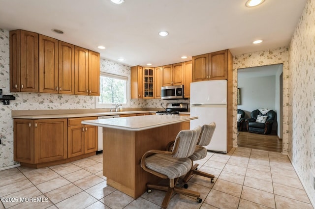 kitchen with appliances with stainless steel finishes, a center island, a sink, glass insert cabinets, and wallpapered walls