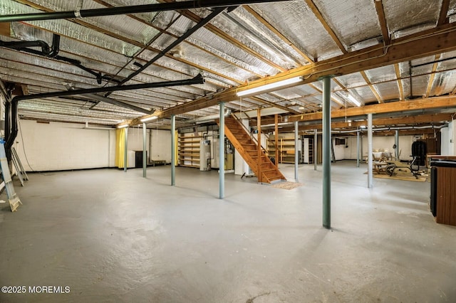 unfinished basement featuring concrete block wall, stairway, and gas water heater