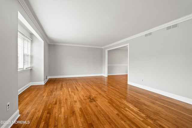 empty room with ornamental molding, wood finished floors, visible vents, and baseboards