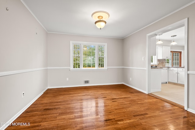 spare room with light wood-style flooring, a healthy amount of sunlight, visible vents, and ornamental molding