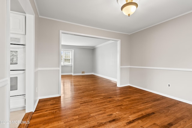 empty room with crown molding, baseboards, and wood finished floors