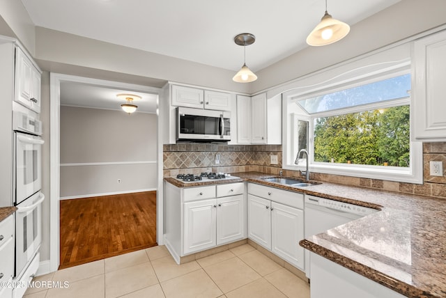 kitchen featuring white appliances, light tile patterned floors, a sink, white cabinetry, and backsplash