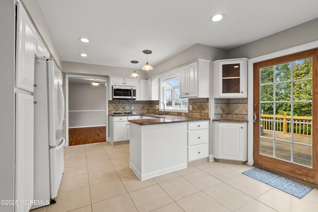 kitchen with stainless steel microwave, a peninsula, freestanding refrigerator, and white cabinetry