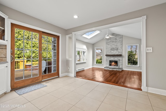 unfurnished living room with tile patterned floors, lofted ceiling with skylight, a ceiling fan, baseboard heating, and a healthy amount of sunlight