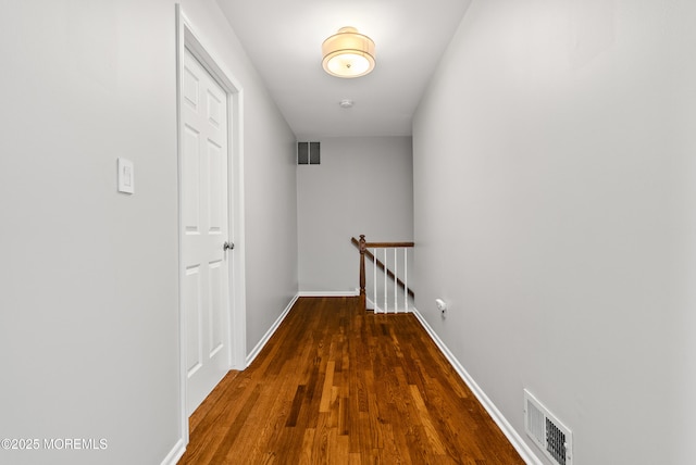 hall featuring visible vents, an upstairs landing, baseboards, and wood finished floors