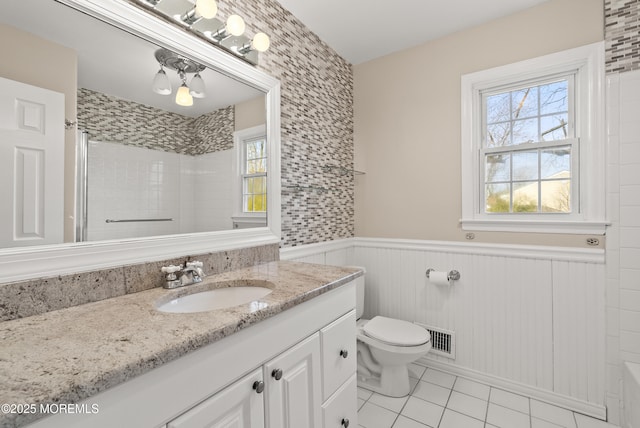 full bathroom featuring visible vents, a wainscoted wall, toilet, vanity, and a shower