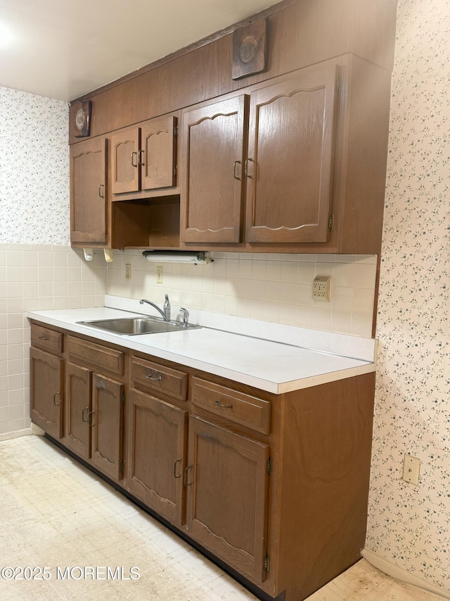 kitchen with wallpapered walls, light countertops, a wainscoted wall, and a sink