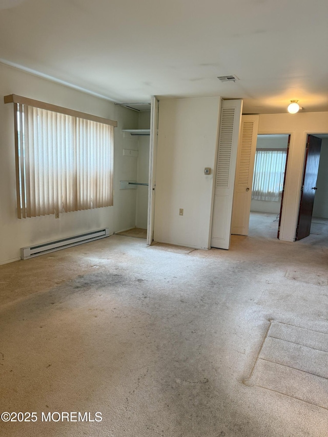 unfurnished bedroom featuring two closets, visible vents, baseboard heating, and carpet flooring