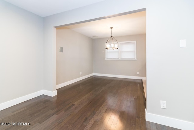 empty room with a notable chandelier, baseboards, and dark wood-style flooring