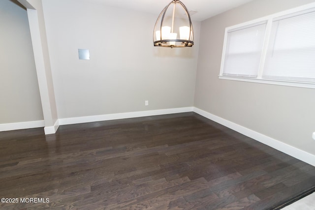 unfurnished dining area with dark wood finished floors, a notable chandelier, and baseboards