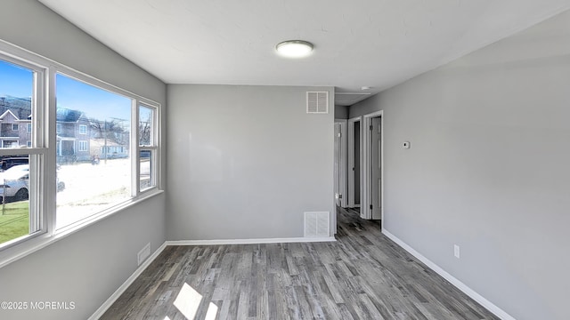 spare room with wood finished floors, visible vents, and baseboards