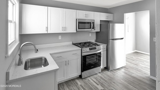 kitchen with light stone countertops, light wood-style flooring, a sink, stainless steel appliances, and white cabinetry