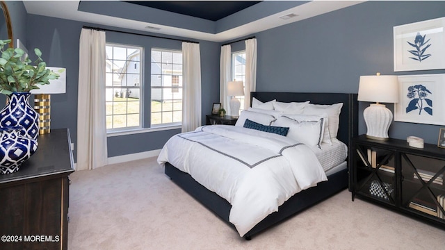 bedroom with a tray ceiling, visible vents, baseboards, and carpet