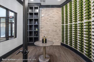 wine area with wood finished floors, baseboards, brick wall, and ornamental molding