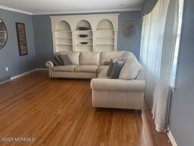 living room featuring built in features, wood finished floors, visible vents, baseboards, and ornamental molding