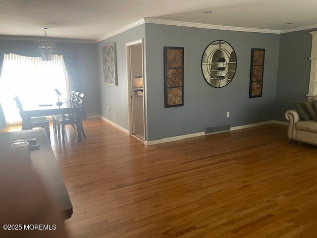 interior space with an inviting chandelier, crown molding, wood finished floors, and visible vents