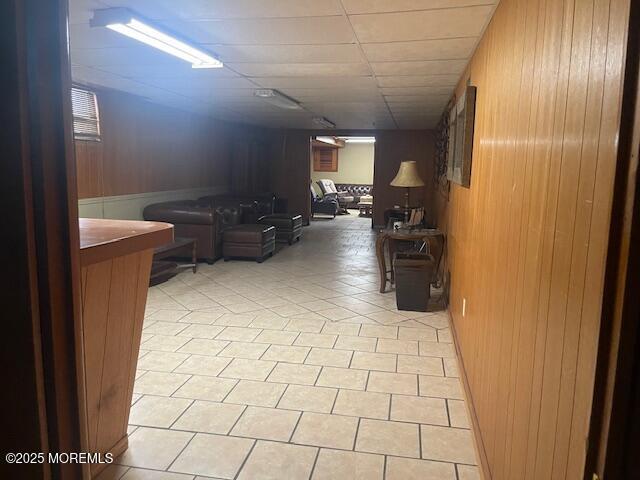 corridor featuring light tile patterned floors, a drop ceiling, and wood walls