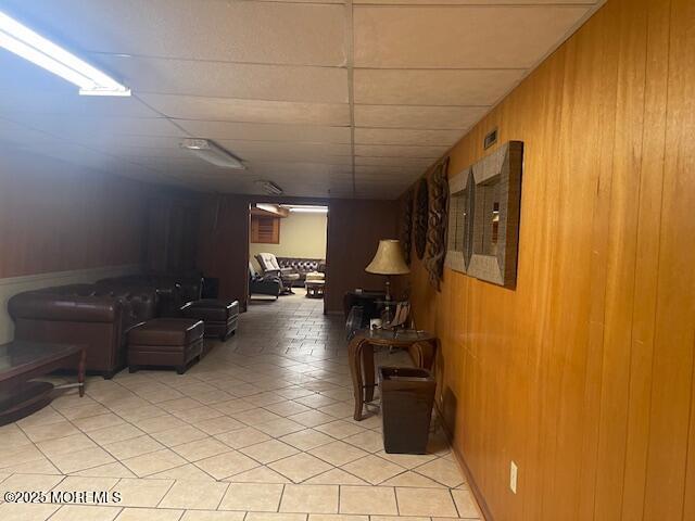 hallway featuring light tile patterned floors, a drop ceiling, and wood walls