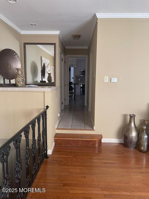 hallway with baseboards, wood finished floors, and crown molding