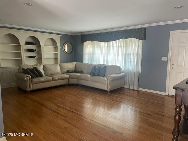 living room featuring built in features, baseboards, dark wood-style floors, and crown molding