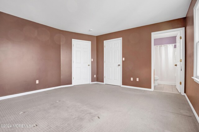 unfurnished bedroom with baseboards, ensuite bathroom, and carpet flooring