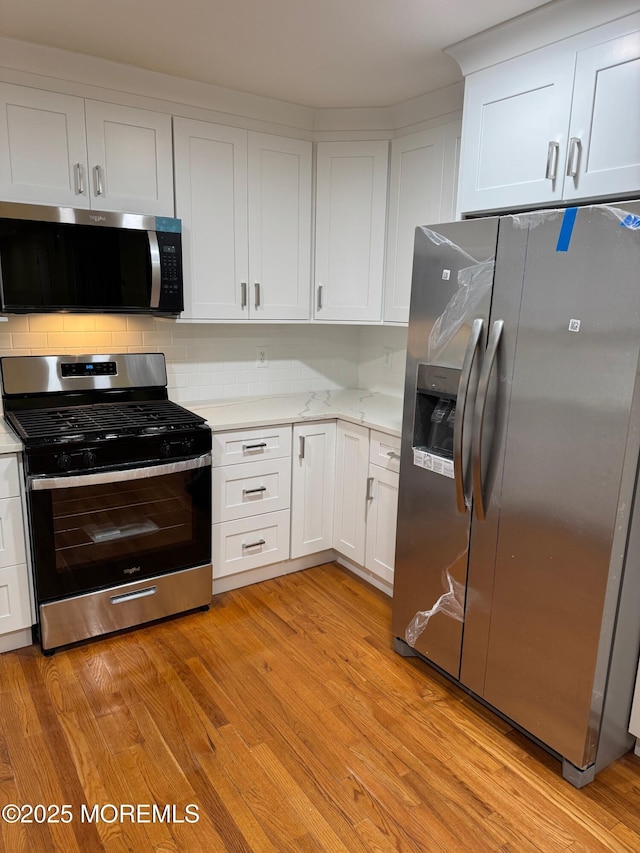 kitchen featuring decorative backsplash, light wood-style flooring, white cabinets, and stainless steel appliances