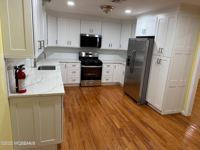 kitchen featuring visible vents, a sink, wood finished floors, appliances with stainless steel finishes, and white cabinets