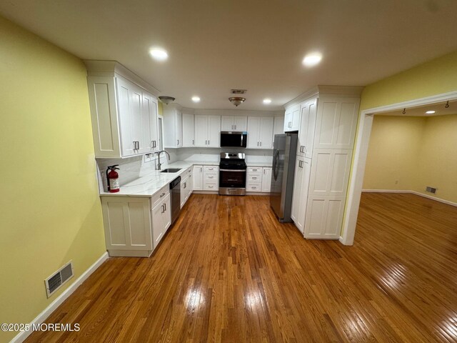 kitchen featuring baseboards, visible vents, white cabinets, wood-type flooring, and appliances with stainless steel finishes