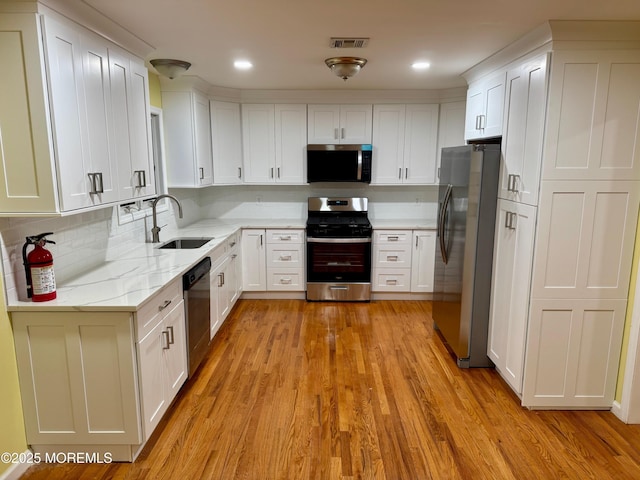 kitchen with visible vents, appliances with stainless steel finishes, light wood-style floors, white cabinetry, and a sink