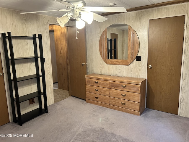 unfurnished bedroom featuring light colored carpet, wood walls, and a ceiling fan