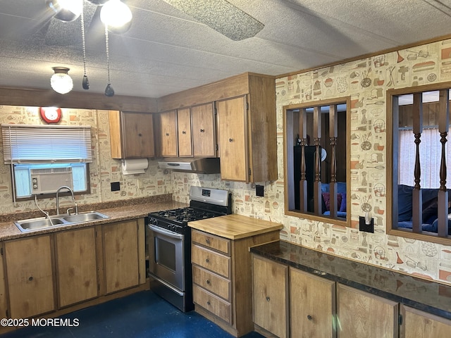 kitchen with gas stove, brown cabinets, under cabinet range hood, and a sink