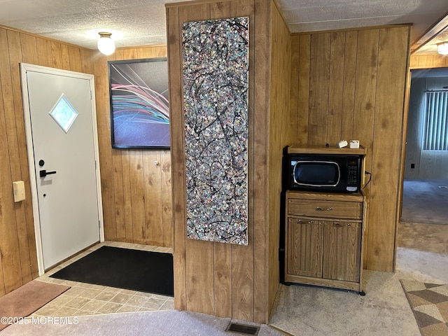 kitchen with wooden walls, visible vents, carpet flooring, and black microwave