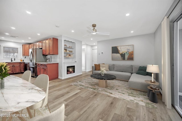 living room featuring visible vents, light wood finished floors, recessed lighting, a ceiling fan, and a glass covered fireplace