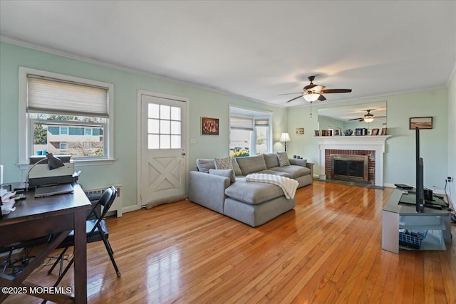 living area with a brick fireplace, light wood-type flooring, crown molding, and a ceiling fan