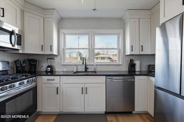 kitchen with a sink, dark countertops, white cabinets, and stainless steel appliances