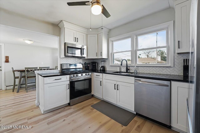 kitchen featuring a ceiling fan, light wood-style flooring, a sink, appliances with stainless steel finishes, and dark countertops