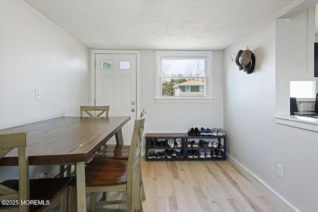 dining area with light wood finished floors, a textured ceiling, and baseboards