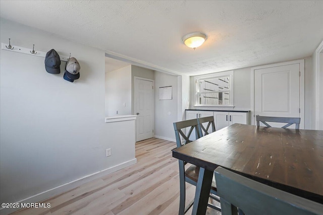 dining space featuring light wood-style flooring, a textured ceiling, and baseboards