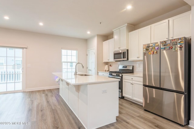 kitchen featuring an island with sink, decorative backsplash, light wood-style flooring, stainless steel appliances, and a sink