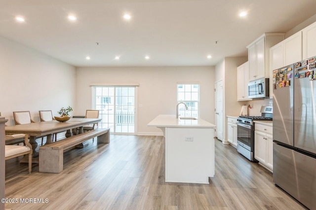 kitchen featuring white cabinets, a kitchen island with sink, light wood finished floors, and stainless steel appliances